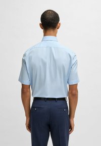 Camicetta a maniche corte di colore azzurro chiaro realizzata in tessuto morbido, caratterizzata da un colletto classico e un design posteriore pulito, abbinata a pantaloni scuri.