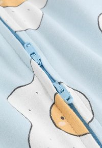 Ljusblått tyg med vita och gula äggmönster; har en blå dragkedja längs mitten. Mjukt, texturerat material.