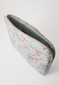 Blomsterprintet lynlåspose med en lys blå yderflade, guldlås og en glat satinlignende indvendig foring. Den har lyserøde og hvide blomster.