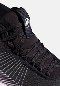 Mustvalge sportkinga lähipilt, millel on tekstureeritud kootud pealne, ristatud paelad ning must tõmbenööp, millel on valge mammuti logo.