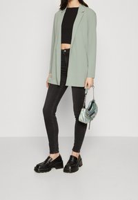 Jasnozielona marynarka, czarny crop top, czarne obcisłe dżinsy, masywne czarne loafersy oraz mała, iryzująca torebka na łańcuszku.