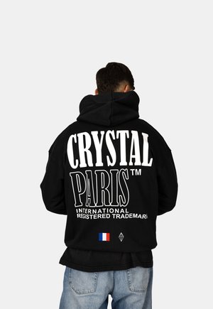 Černá mikina s kapucí, na zadní straně velký bílý nápis "CRYSTAL PARIS™", s malou francouzskou vlajkou a akcentem loga diamantu dole.