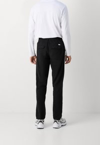 Zwarte broek met een relaxte pasvorm, elastische tailleband en achterzakken, gecombineerd met een wit longsleeve shirt en grijze sneakers.