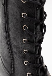 Svart läderboot med metallöglor, svarta snören och en sidodragkedja för stängning. Strukturerad yta synlig bredvid snörningsdetalj.