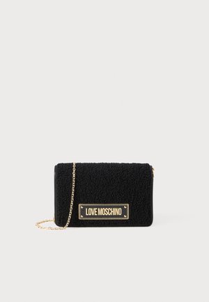 Čierna plyšová kabelka s textúrovaným povrchom, zlatým reťazovým popruhom a zlatou logovou destičkou vpredu. Kompaktný obdĺžnikový tvar.