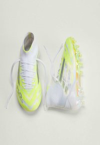 Φωτεινά κίτρινα και λευκά παπούτσια ποδοσφαίρου με λυτά κορδόνια, που εμφανίζουν σχεδιασμό με ψηλές κάλτσες στον αστράγαλο και σόλα με καρφιά σε ένα παπούτσι.