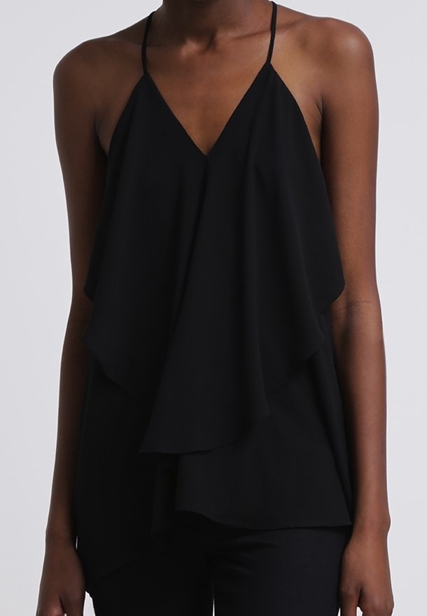 Femme portant un haut noir sans manches avec des fines bretelles et un tissu amples superposé à l'avant.