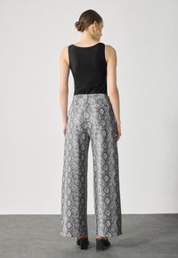 Zwarte mouwloze top gecombineerd met brede grijze broek met slangenprint, voorzien van een textuurpatroon en effen zwarte hakken.