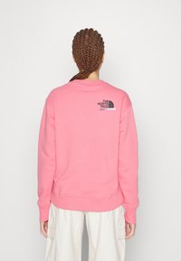 Felpa rosa con scollo a girocollo, polsini e vita a costine. Presenta un piccolo logo nero sulla parte superiore della schiena. Tessuto morbido in misto cotone.
