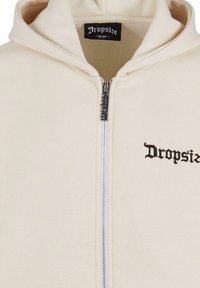 Creme zip-up hoodie lavet af blødt stof, med en frontlynlås og sort "Dropsize" logo på venstre brystområde.