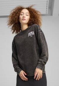 Čierny, opotrebovaný sveter s dlhými rukávmi, okrúhlym výstrihom a bielym vyšívaným logom s nápisom "PUMA sports club." Mäkkučký, textúrovaný materiál.