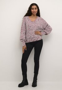 Pulover tricotat roz și gri cu decolteu în V, cu manșete cu nervuri și croială lejeră, asortat cu blugi skinny negri și botine.