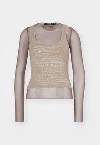 Débardeur beige associé à des manches longues en maille ; présente une impression en écriture blanche sur le devant, un col rond et une silhouette ajustée.