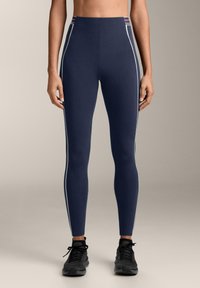 Tengerészkék leggings fehér oldalsávokkal és színes részletekkel a deréknál. Rugalmas anyagból készült, szoros illeszkedéssel és sima textúrával.