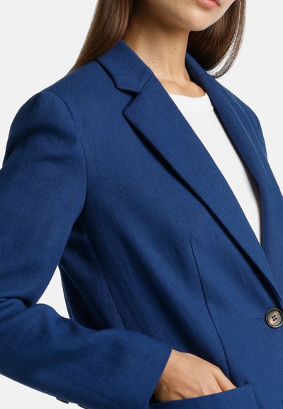 Blue blazer made of textured fabric, featuring a notched lapel, single button closure, and front pockets. Tailored fit with structured shoulders.