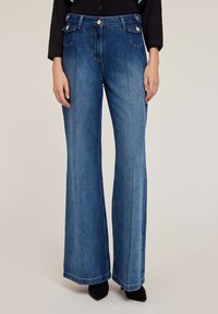 Szerokie dżinsy o prostym kroju w ciemnoniebieskim kolorze, o gładkiej fakturze, z przednimi kieszeniami, złotymi guzikami oraz prostą linią ku dołowi.