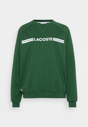 Felpa verde con scollatura rotonda, polsini e orlo a costine. Presenta il logo "LACOSTE" in bianco sulla parte anteriore e un piccolo logo sul lato.