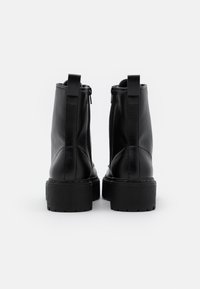 Pár černých kožených kotníkových bot s robustními podrážkami a zadními poutky, zobrazených ze zadní strany na jednoduchém bílém pozadí.