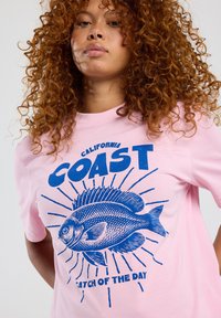 Pink cotton t-shirt featuring a blue graphic of a fish with "CALIFORNIA COAST" and "CATCH OF THE DAY" text. Short sleeves and crew neck.