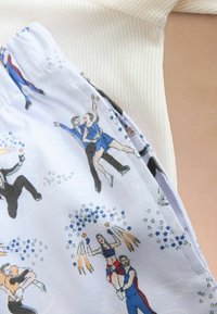 Primer plano de una tela con ilustraciones impresas de patinadores artísticos realizando elevaciones y giros, vestidos con coloridos trajes sobre un fondo blanco.