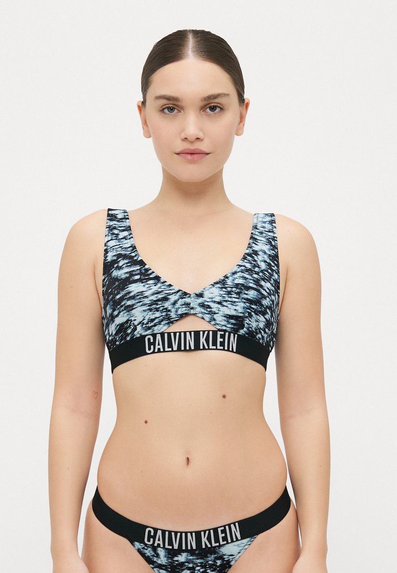 Calvin Klein komplet grudnjaka i bikinija s apstraktnim uzorkom u plavoj i crnoj boji. Mekani materijal, široke naramenice i detalj u vidu logotipa na pojasu.
