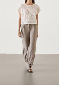 Haut en dentelle écrue mélangée en lin, court, avec motif floral ; pantalon ample gris clair à coupe droite ; sandales plates noires.