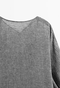 Maglione grigio a maglia con scollatura a V, maniche larghe e tessuto testurizzato. Il motivo a maglia aggiunge profondità e interesse al capo.