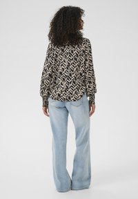 Blouse noire et crème à motifs avec des manches bouffantes, associée à un jean flare taille haute bleu clair, avec une finition en denim classique.