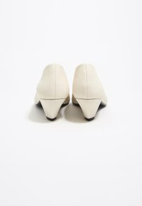 Zapatos de tacón alto de cuero blanco con punta afilada, un tacón bajo en forma de cono y una textura suave. Detalles de la suela en negro.