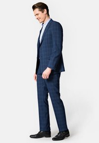Granatowy garnitur w kratę z dopasowaną marynarką i spodniami. Gładka tekstura i subtelny wzór. Uzupełniony czarnymi eleganckimi butami.