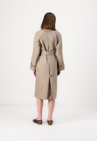 Beige Trenchcoat mit tailliertem Schnitt, langen Ärmeln und Knopfdetails. Verfügt über eine Rückenschlitz für Bewegungsfreiheit. Getragen mit Schuhen im Leopardenmuster.