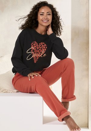 Schwarzer Sweatshirt mit einem Leopardenherzen-Muster und dem Wort "Smile" in Gold. Kombiniert mit rostfarbenen Sweatpants mit umgeschlagenen Bündchen und einem Kordelzug.