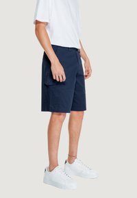 Pantaloni cargo navy realizzati in tessuto leggero, con tasche laterali e vestibilità regolare, abbinati a sneakers bianche e una t-shirt bianca.