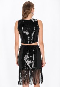 Fekete flitteres rövid felső testhezálló fazonban. Egy hozzáillő szoknyával párosítva, amelyen rojtos részletek találhatók az alján. Sima textúra, fényes felület.