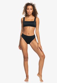 Set di bikini nero caratterizzato da un reggiseno a scollo quadrato con spalline larghe e slip a vita alta, realizzato in tessuto elasticizzato testurizzato.