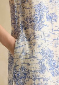 Medvilniniai drabužiai su smėlio spalvos fono, kurį puošia mėlynų peizažų atspaudai, palmės, burlaiviai ir išskirtinės detalės.