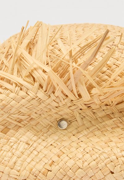 Gros plan sur un chapeau en paille tissée avec des bords effilochés et un petit bouton métallique rond sur le bord.