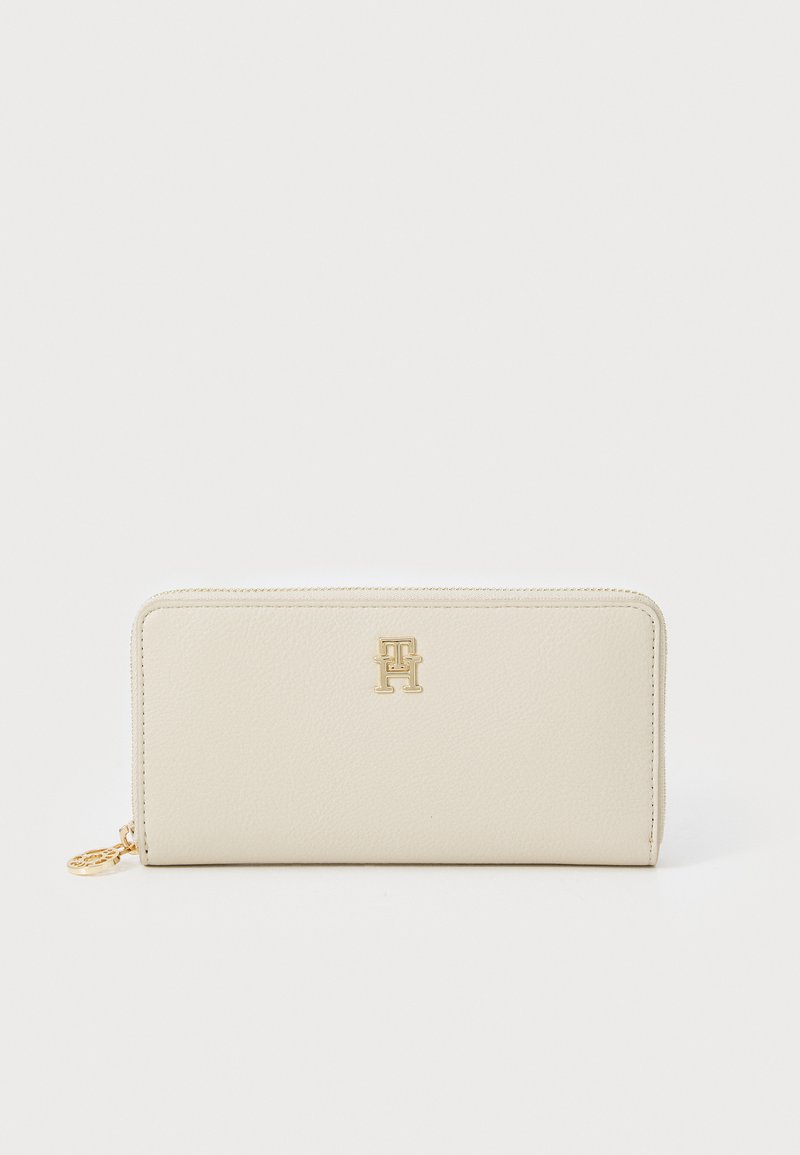 Cremefarbenes Lederportemonnaie mit strukturiertem Finish, goldfarbener Logo auf der Vorderseite und Reißverschluss. Kompaktes rechteckiges Design.