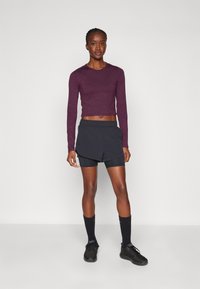 Athletic outfit featuring a cropped, maroon long-sleeve top, black layered shorts, black socks, and black sneakers. Simple design with functional fit.