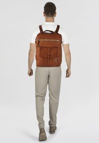 Zaino in pelle marrone con finitura texturizzata, caratterizzato da una tasca frontale con cerniera, spallacci regolabili e una forma rettangolare elegante.