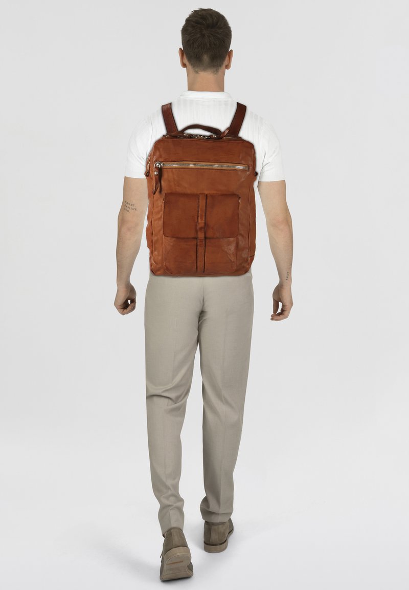 Zaino in pelle marrone con finitura texturizzata, caratterizzato da una tasca frontale con cerniera, spallacci regolabili e una forma rettangolare elegante.