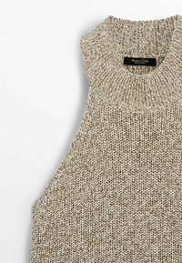 Beige gestricktes ärmelloses Oberteil mit einem hohen gerippten Ausschnitt und einem strukturierten Muster. Der Stoff wirkt weich und leicht dick, ideal zum Schichten.