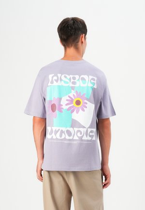 Lavender cotton T-shirt featuring a colorful graphic of flowers and geometric shapes, with "LISBOA UTOPIA" text in bold white font.