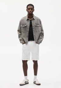 Jachetă din denim gri, cămașă neagră, pantaloni scurți albi cu efect uzat și adidași multi-colorați cu tălpi groase, purtați cu șosete albe.