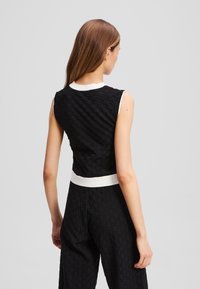 Black textured sleeveless top with a white ribbed waistband, showcasing a geometric pattern and a round neckline.
