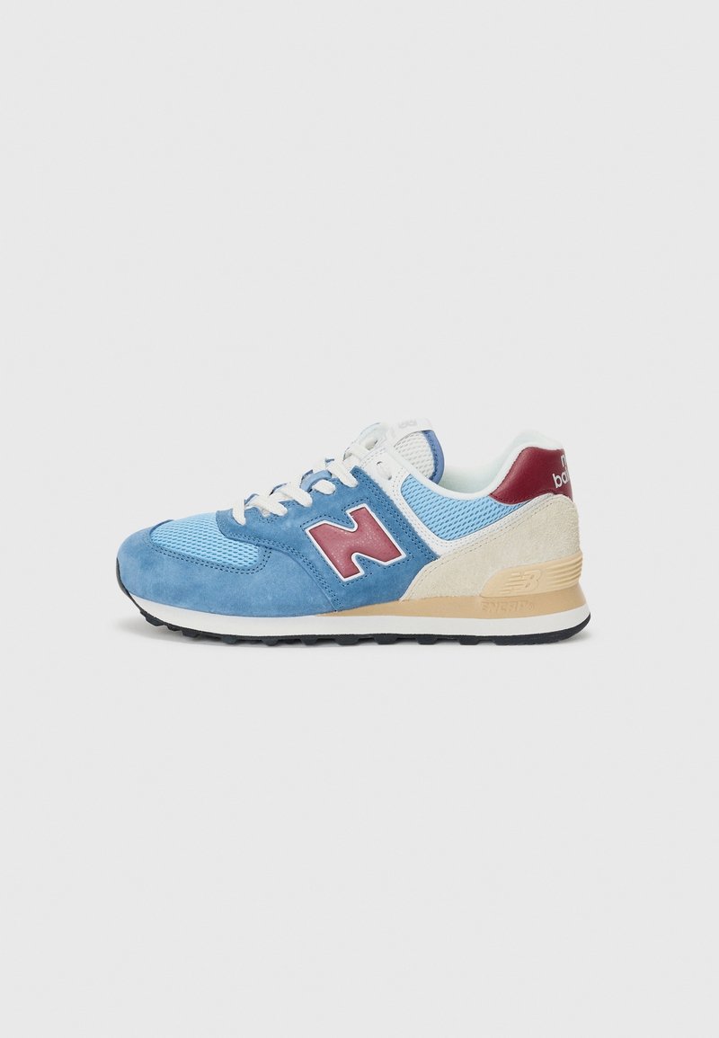 Baskets New Balance bleu et beige avec logo "N" rouge, lacets blancs, textures en mesh et en daim, et semelle noire vues de côté.