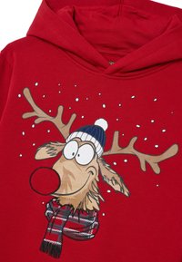 Felpa rossa con cappuccio decorata con un renna di cartone animato con grandi occhi, corna marroni, un cappello di lana blu e una sciarpa a scacchi. Fiocchi di neve sono stampati attorno.