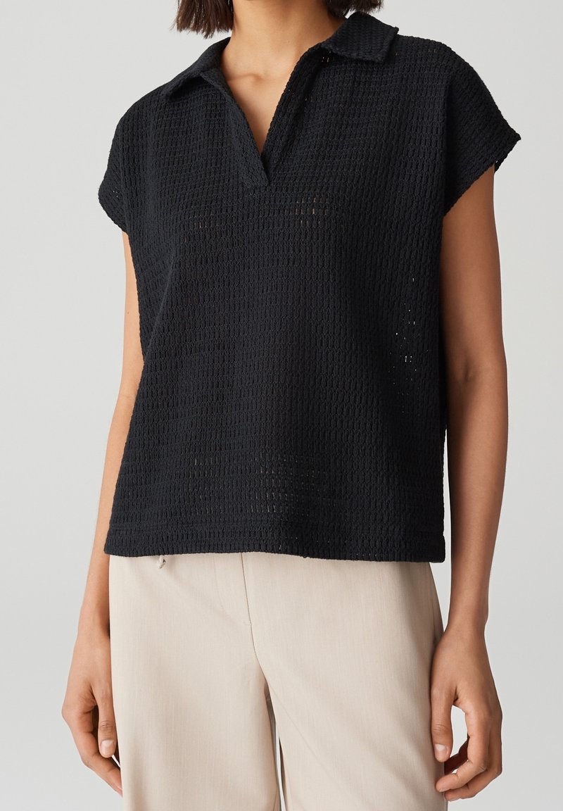 Polo à manches courtes noir avec un motif en maille texturée, doté d'un col et d'une coupe décontractée, assorti à un pantalon beige.