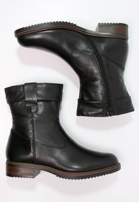 Bottines en cuir noir avec une fermeture éclair sur le côté, bout rond, revers replié et semelle en caoutchouc texturée. Détail de talon en bois marron.