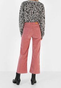 Roze corduroy wijdvallende broek met achterzakken en een leren patch op de tailleband, gecombineerd met een grijze shirt met luipaardprint en zwarte enkellaarsjes.